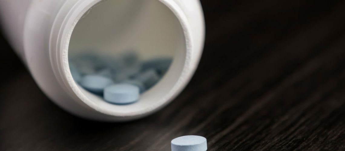 Medication pill in a row against a wood background. White pill bottle